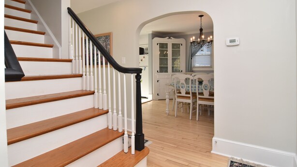 A staircase with wooden steps and white railings, leading to a dining area with a chandelier and a white cabinet.
