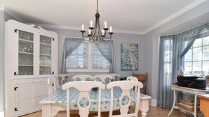 A dining room with a white table and chairs, a chandelier, a cabinet with glass doors, and a window with curtains.