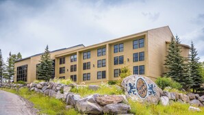 A multi-story building with a beige facade, large windows, and a stone pathway leading to a decorative rock with the text "Regal Crest". - Ski In/Ski Out Studio - Perfect Get Away (Brian Head)