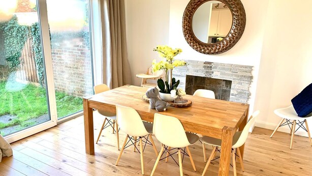 A dining area with a wooden table, white chairs, a round mirror, and a potted plant.