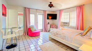A bedroom with a bed, a chair, a TV, and a window with curtains.