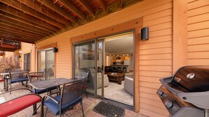 Un patio exterior con una parrilla, una mesa de comedor con sillas y un ventanal corredero que da a un espacio interior.