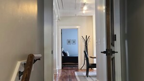 Un pasillo con suelo de madera, un perchero y una puerta que da a una habitación con cama y sillón.