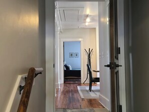 Un pasillo con piso de madera, un perchero y una puerta que da a una habitación con cama y sillón.