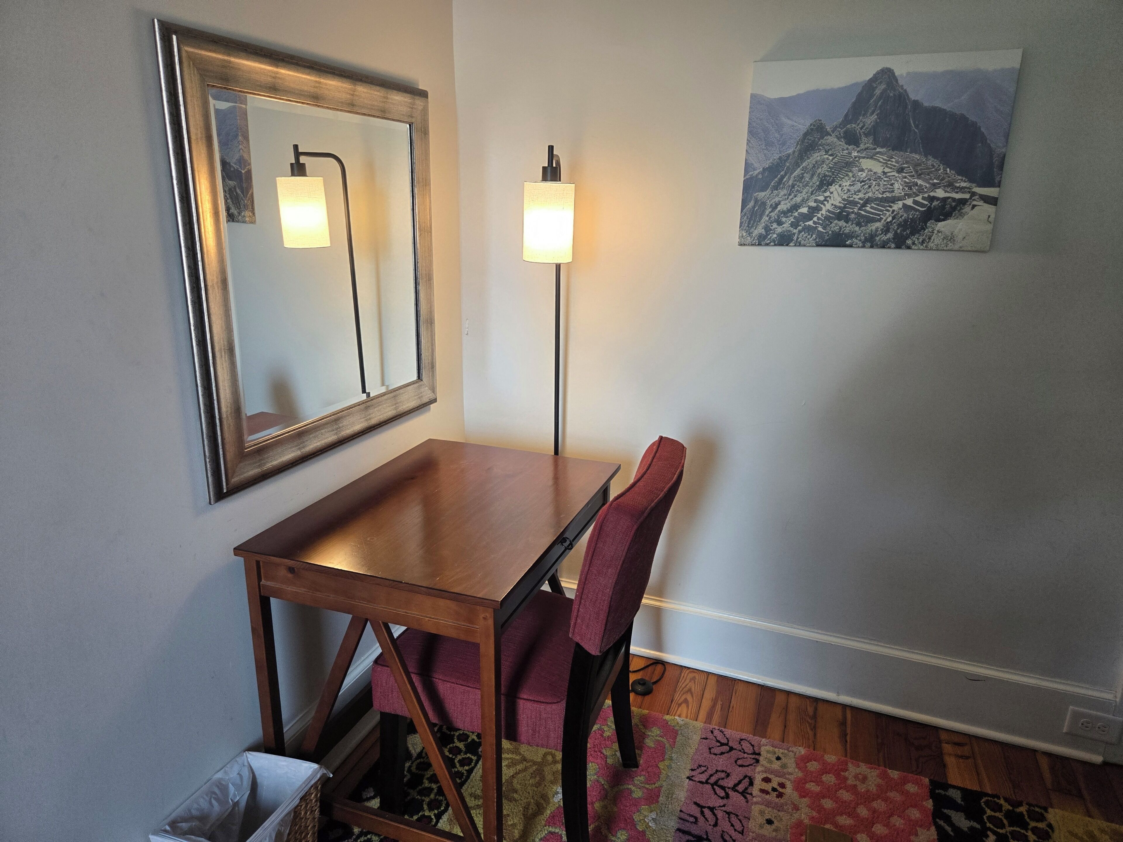 Un coin repas avec une table en bois, une chaise, un miroir, un lampadaire et un tableau encadré accroché au mur.