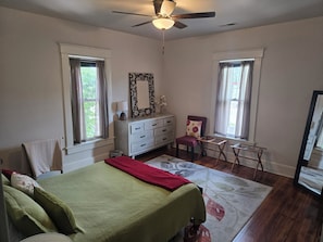 A bedroom with a bed, dresser, chair, and a ceiling fan.