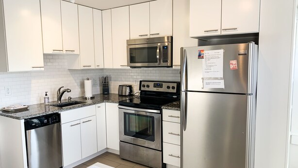 Una cocina moderna con electrodomésticos de acero inoxidable, armarios blancos y encimera de granito.