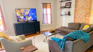 Una sala de estar con sofá, sillón, mesa de centro y televisor sobre un mueble.