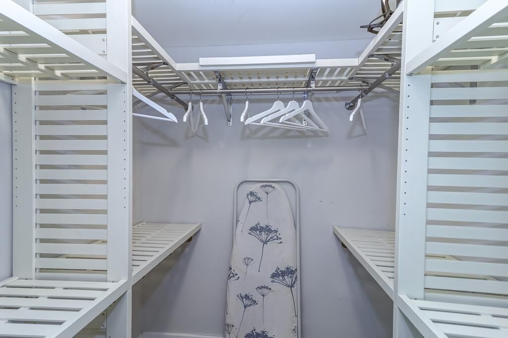 A walk-in closet with white shelving units, a hanging rod, and a large ironing board.