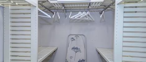 A walk-in closet with white shelving units, a hanging rod, and a large ironing board.