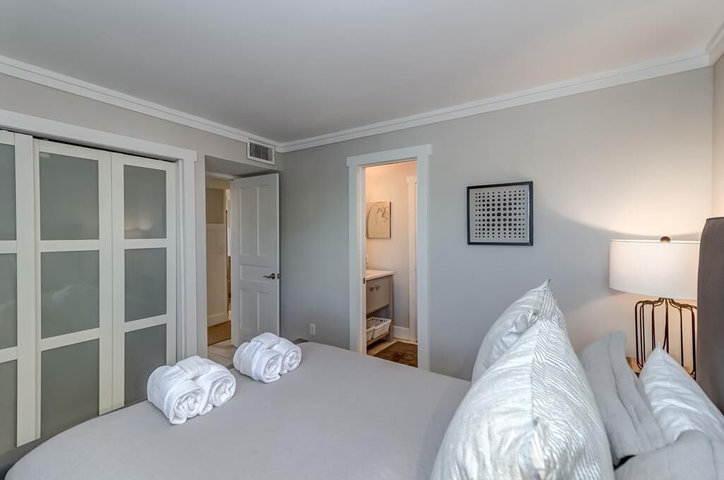 Una habitación de hotel con cama, un armario con puertas de cristal esmerilado, una mesita de noche con lámpara y una obra de arte enmarcada en la pared.