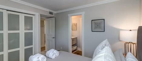Una habitación de hotel con cama, un armario con puertas de cristal esmerilado, una mesita de noche con lámpara y una obra de arte enmarcada en la pared.
