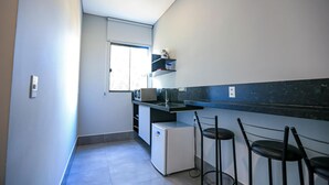 A compact kitchen with a microwave, a small refrigerator, and a window providing natural light. There are two black bar stools near the counter.