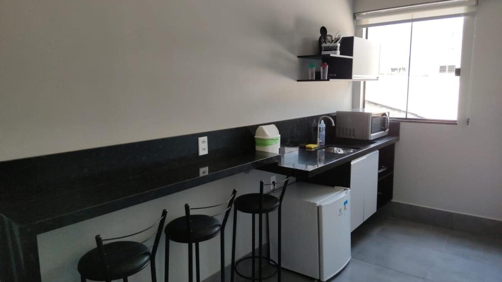 Una cocina compacta con cubierta negra, un refrigerador blanco y tres taburetes negros.