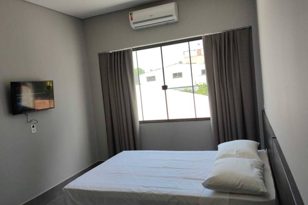 Une chambre d’hôtel avec un lit, un téléviseur fixé au mur et une fenêtre avec des rideaux.