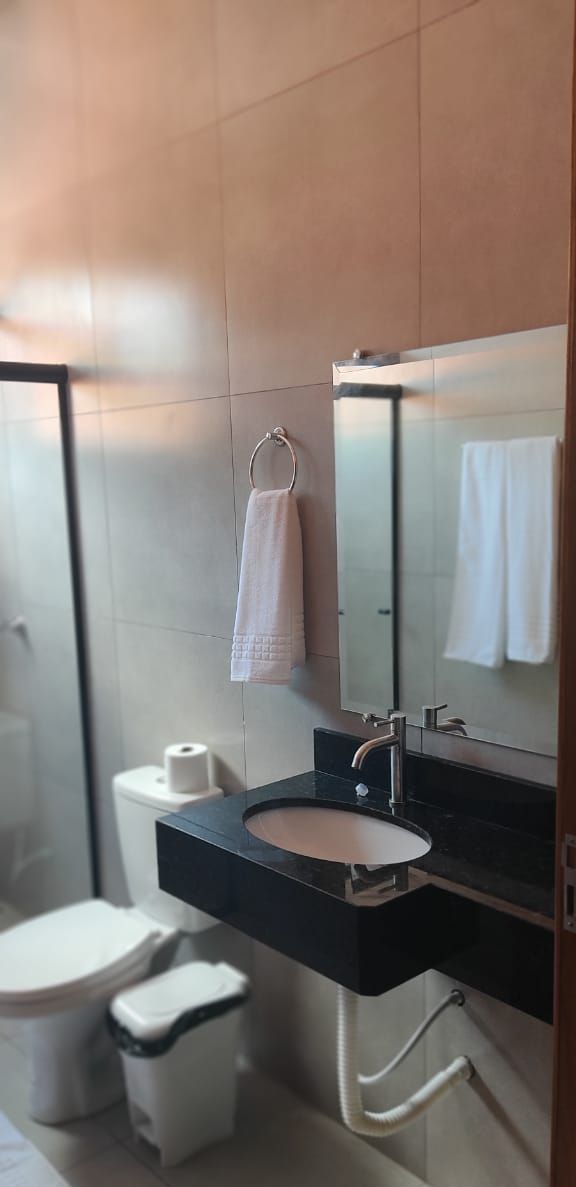 A modern bathroom with a black sink, a mirror, a towel rack, a toilet, and a trash bin.