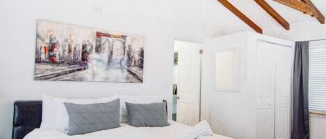 Un dormitorio con una cama grande, vigas de madera, un ventilador de techo y un cuadro de un paisaje urbano.
