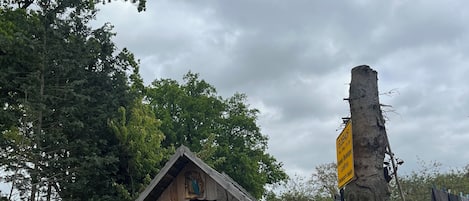 A rustic wooden cabin with a sloped roof, a bench in front, and a sign on a tree.
