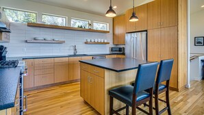 Een moderne keuken met houten kastjes, een roestvrijstalen koelkast en een centraal kookeiland met barkrukken.