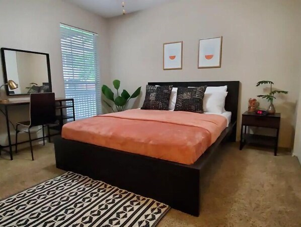 Une chambre à coucher avec un lit, un bureau, une chaise, une plante et une table de chevet.
