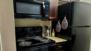 A compact kitchen with a black stove, microwave, and refrigerator. There are two hanging pots and a utensil holder on the countertop. - Cozy Condo - Pond View - Monthly Discounts- Washer & Dryer-Great Location (Lombard)