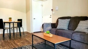 A living room with a sofa, a coffee table, a dining table with chairs, and a door. - Cozy Condo - Pond View - Monthly Discounts- Washer & Dryer-Great Location (Lombard)