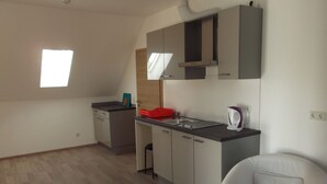 A modern kitchen with a dishwasher, a sink, and a kettle. There is a window providing natural light and a chair in the room. - MyHome10, Wiesbaden - Mainz (Wiesbaden)