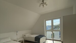 A bedroom with two beds, a ceiling fan, and a large window with a city view. - MyHome10, Wiesbaden - Mainz (Wiesbaden)