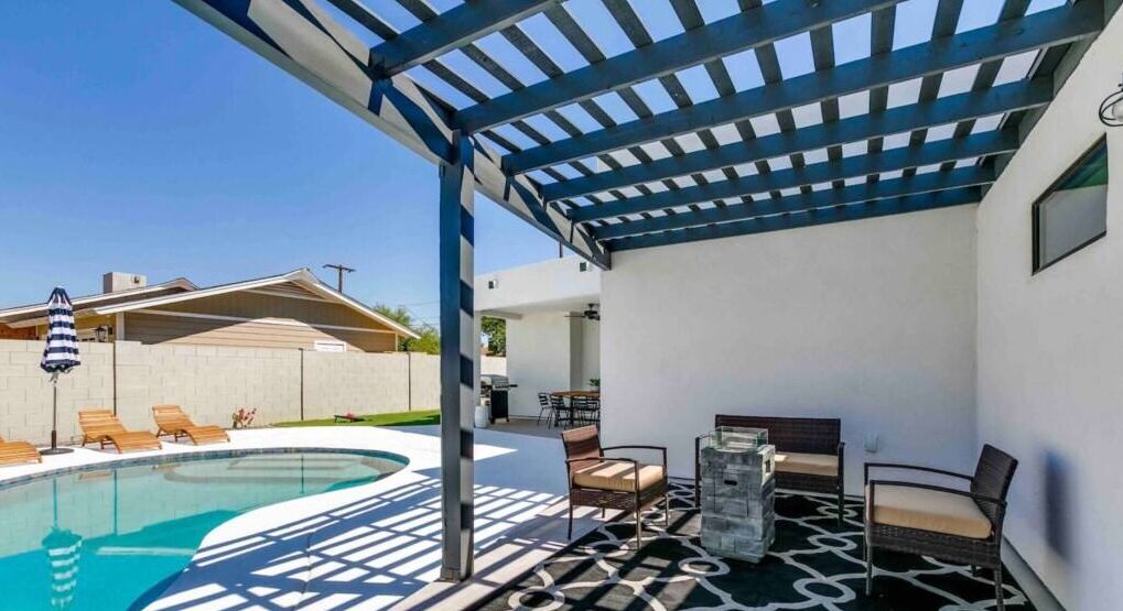 A covered outdoor area with a pool, lounge chairs, and a table with chairs.