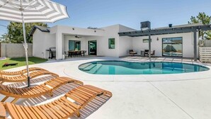 A modern outdoor pool area with wooden loungers and a covered patio. - Luxurious Old Town Remodel Home W/ Heated Pool (Scottsdale)