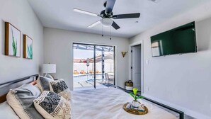 A modern bedroom with a bed, a ceiling fan, a TV, and a view of a pool and outdoor area. - Luxurious Old Town Remodel Home W/ Heated Pool (Scottsdale)