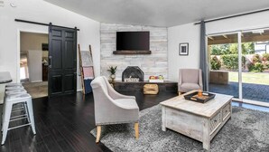 Ein modernes Wohnzimmer mit Kamin aus Stein, einem großen darüber montierten Fernseher und einer Schiebetür zu einem Garten.