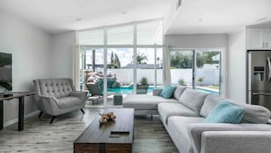 Ein modernes Wohnzimmer mit einem grauen Sofa, einem Holztisch und einer großen Glasdoor zu einem Poolbereich.