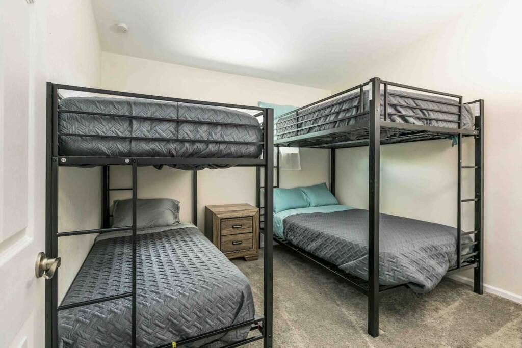 Une chambre avec deux lits superposés, une petite table de chevet en bois et un mur de couleur bleu clair.