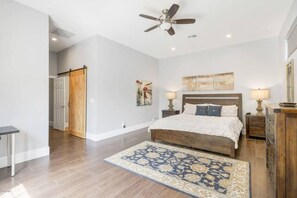 Une chambre à coucher avec un lit, deux tables de chevet, un ventilateur de plafond et une porte en bois.