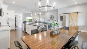 A modern kitchen with white cabinets, a central island, and a dining area with a wooden table and chairs. - New Remodel In Old Town W/ Heated Pool (Scottsdale)