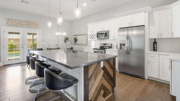 A modern kitchen with white cabinets, stainless steel appliances, a large island with bar stools, and pendant lighting. - New Remodel In Old Town W/ Heated Pool (Scottsdale)