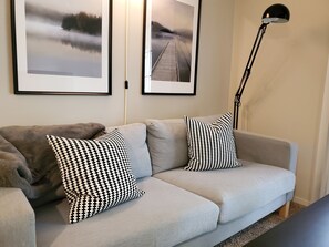 A light grey sofa with two black and white checkered pillows, a black floor lamp, and two framed pictures on the wall.