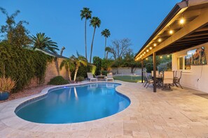 Una piscina de borde curvo, rodeada por un patio con sillas y una mesa.