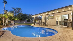 Ein Pool mit Liegefläche, Gartenmöbeln und einem Grill.