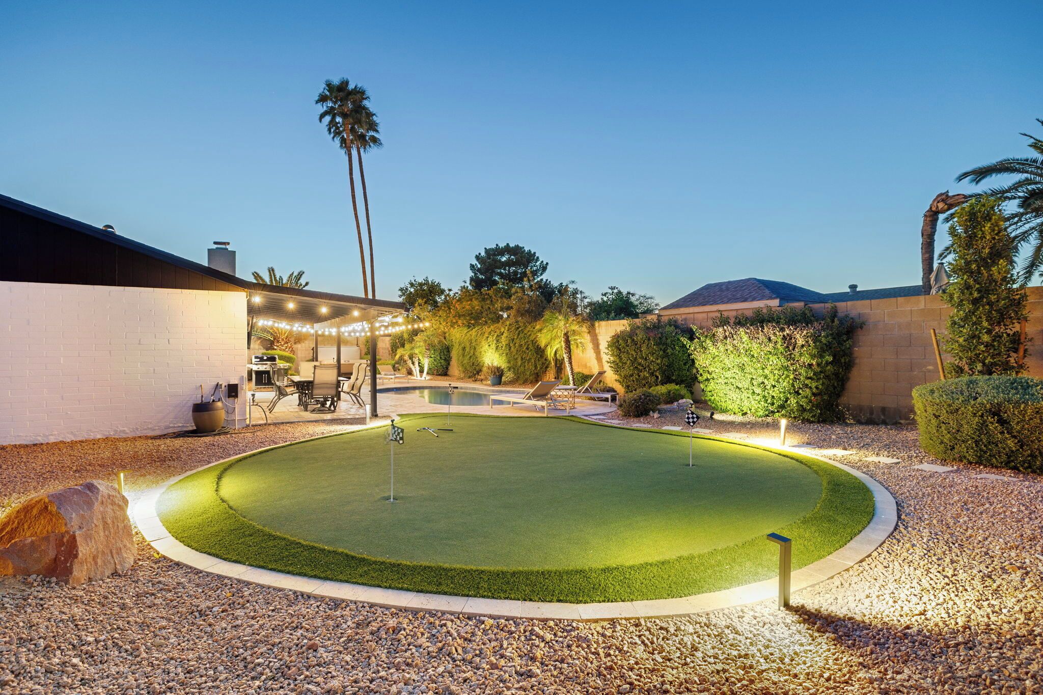 A well-maintained backyard with a pool, a barbecue area, and a small putting green.