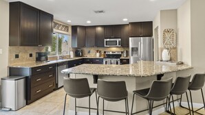 Eine moderne Küche mit dunklen Schränken, Granit-Arbeitsplatten, Edelstahlgeräten und einer Kochinsel mit Barhocker.