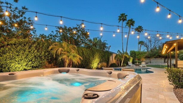 Ein Whirlpool mit einer gefliesten Terrasse, umgeben von Grün und Palmen, unter Lichterketten.
