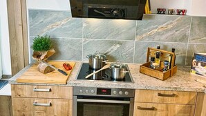 Una cocina con horno integrado, microondas y fogones. Hay armarios de madera, una encimera con tabla de cortar y una pequeña planta.