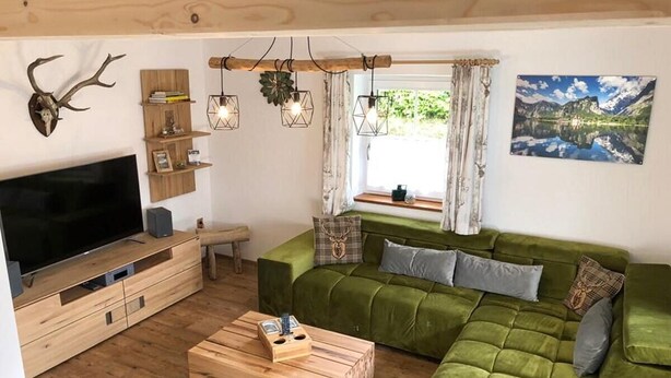 Una sala de estar acogedora con un sofá verde, una mesa de centro de madera y un televisor montado.