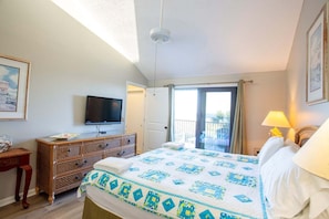 A hotel room with a bed, a television, a dresser, a balcony with a view, and a door leading outside.
