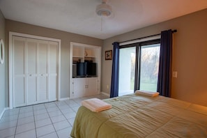A bedroom with a bed, a television on a cabinet, and a sliding glass door to the outside.