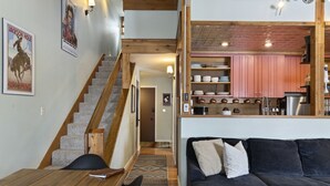 Un intérieur moderne avec un escalier, un canapé foncé et un coin cuisine doté de meubles roses.