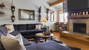 Un salon chaleureux avec un canapé bleu foncé, une cheminée et divers objets décoratifs disposés sur des étagères et accrochés aux murs.