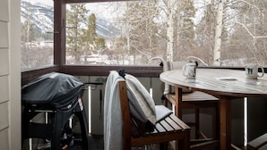 Une terrasse en bois avec une table et des chaises, donnant sur un paysage enneigé parsemé d’arbres et de montagnes.